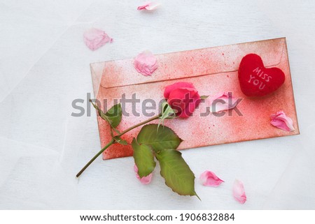 Valentine's Day background: pink rose, pink rose petals,plush heart "Miss you",a red envelope on a transparent fabric.
