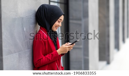 Banner panorama. Portrait Young Asian muslim woman  in hijab and sending massaging on mobile phone on city street outdoor.