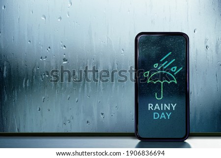 Rainy Day Concept. Weather Information Forecast show on Mobile Phone Screen. View from Inside, through Glass Window