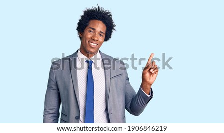 Handsome african american man with afro hair wearing business jacket with a big smile on face, pointing with hand finger to the side looking at the camera. 
