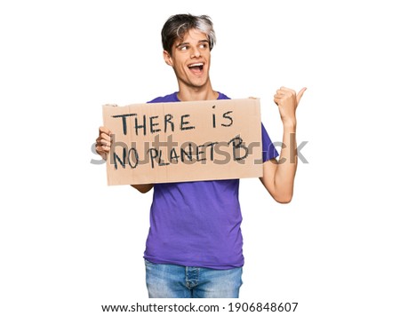 Young hispanic man holding there is no planet b banner pointing thumb up to the side smiling happy with open mouth 