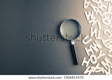 Magnifying glass with part of scattered Engligh alphabt letters on the table