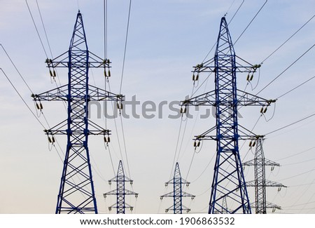 High voltage power lines pylons and electrical cables on a clear blue sky background. Modern infrastructure of high voltage transmission lines. Overhead power lines towers equipment. Energy industry. Royalty-Free Stock Photo #1906863532