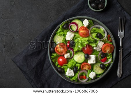 Fresh greek salad with olives, feta cheese, tomato, cucumber, onion with fork on towel on black background. top view. vegetarian food Royalty-Free Stock Photo #1906867006