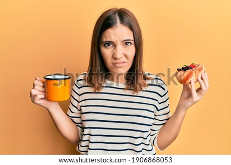 Young beautiful woman drinking coffee and eating pastry skeptic and nervous, frowning upset because of problem. negative person. 