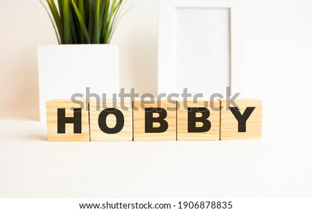 Wooden cubes with letters on a white table. The word is HOBBY. White background with photo frame, house plant.