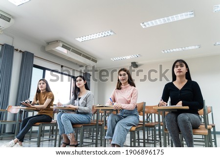 Selective focus of the teen college students sitting on lecture chair in classroom write on examination paper answer sheet in doing the final examination test. Female students in the student uniform.