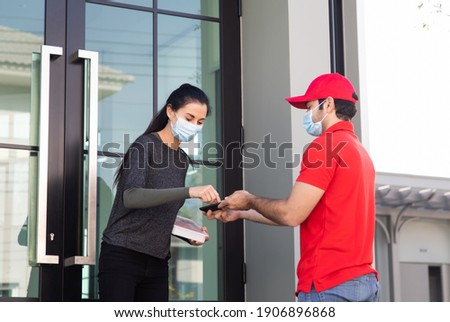 Signing signature on smart phone device to get a package. woman receiving package from delivery man in red uniform . Protection face mask quarantine pandemic coronavirus virus 2019-ncov 