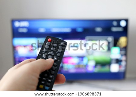 Male hand with remote controller on smart TV screen background. Person choosing streaming services, watching movies