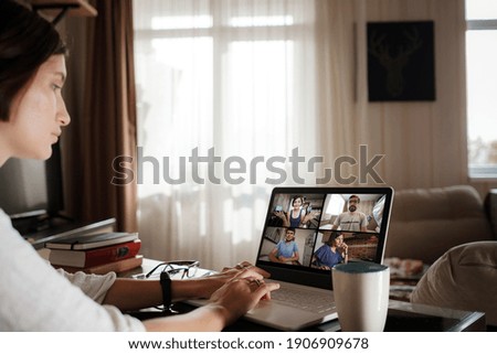 Smiling young asian woman video calling on laptop. Back view photo student looking at computer screen watching webinar or doing video chat by webcam. Over shoulder close up mock up screen view.