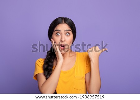 Wow, Look Here. Amazed young indian woman pointing at copy space over purple studio background. Excited surprised lady indicating free space, showing place for advert or promotional text Royalty-Free Stock Photo #1906957519