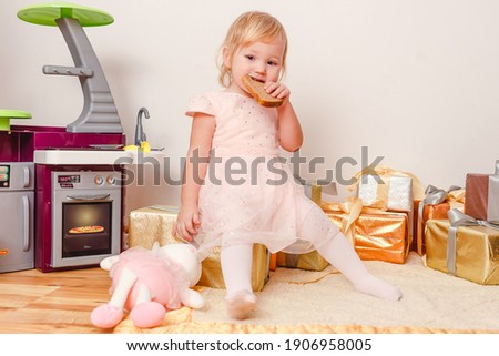 Little girl in pink dress sits and eats bread at home