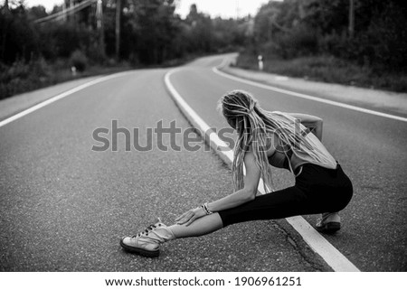 A woman warms up before jogging on the road. Black and white photo.
