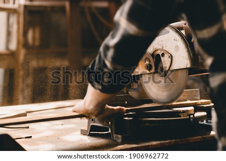 Carpenter using Electric Wood Cutter making wooden furniture in DIY workshop. Royalty-Free Stock Photo #1906962772