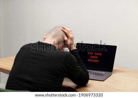 Red text on a laptop saying ‘You have been hacked’. A desperate man sitting in front of his infected computer. Cybercrime, infected unsafe device
