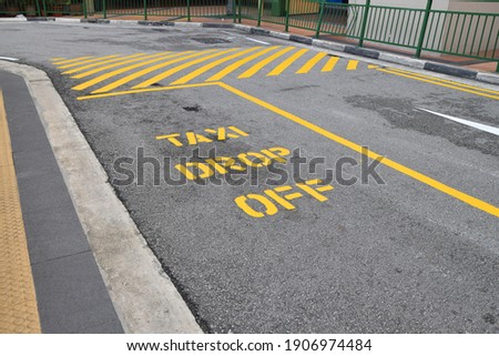 Taxi drop off point parking space sign on black asphalt tarmac in large yellow letters  