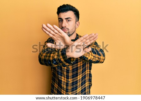 Young hispanic man wearing casual clothes rejection expression crossing arms and palms doing negative sign, angry face 