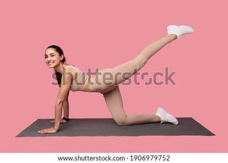 Body Shaping Workout. Smiling Fit Young Woman In Sportswear Doing Exercise With Leg Raise On Yoga Mat Isolated Over Pink Studio Background. Full Length, Banner. Sport And Fitness Concept Royalty-Free Stock Photo #1906979752