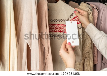 Woman customer looking on tag choosing sweater with christmas ornament in garment store. Shopping. Winter