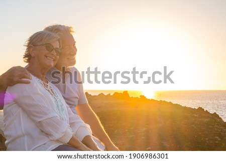 couple of two cute seniors together enjoying summer and having fun at the beach looking at the sea or ocean with sunset - mature people having a good lifestyle Royalty-Free Stock Photo #1906986301
