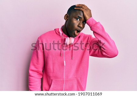 Young african american man wearing gym clothes and using headphones surprised with hand on head for mistake, remember error. forgot, bad memory concept. 