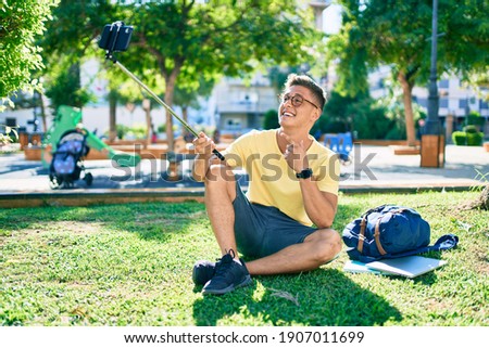 Young hispanic student smiling happy making selfie by the smartphone sitting at the university campus