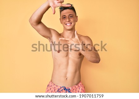 Young hispanic boy wearing swimwear shirtless smiling making frame with hands and fingers with happy face. creativity and photography concept. 