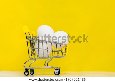 three large eggs in a supermarket cart on a yellow background close-up with space for text on the side
