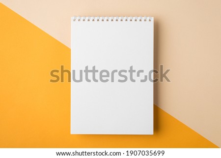 Minimal style note pad. Above overhead close up flat lay photo of clear spiral notepad with copy place for design isolated half yellow and beige backdrop desktop Royalty-Free Stock Photo #1907035699