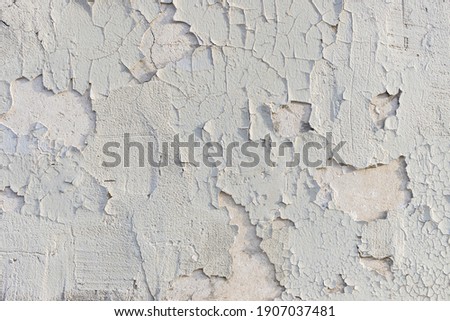Badly fixed white building facade wall covered with cracks in stucco and painting. Very flaky texture. Exposed substrate. Missing patches of paint. Royalty-Free Stock Photo #1907037481