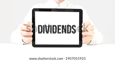 Text dividends on tablet display in businessman hands on the white bakcground. Business concept