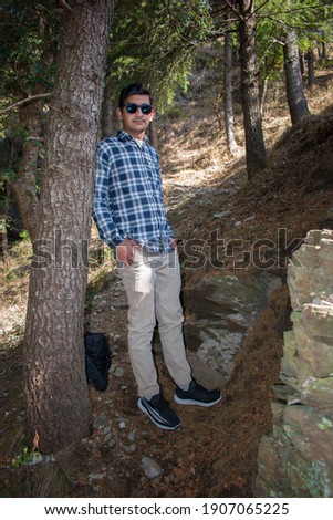 picture of indian boy standing with tree's trunk and hands in pocket.