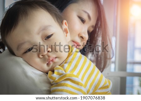 An Asian boy was crying with sad face expression, being carry and hug by his mother to calm down. The child (toddler, kid) cries because of discomfort from sick fever. Royalty-Free Stock Photo #1907076838