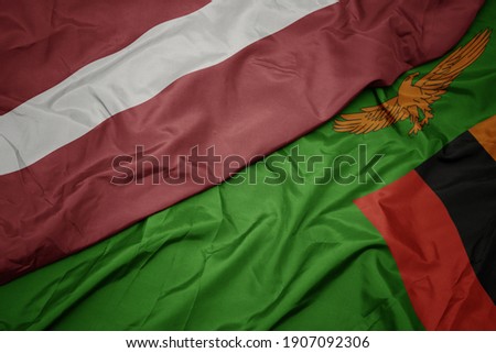 waving colorful flag of zambia and national flag of latvia. macro