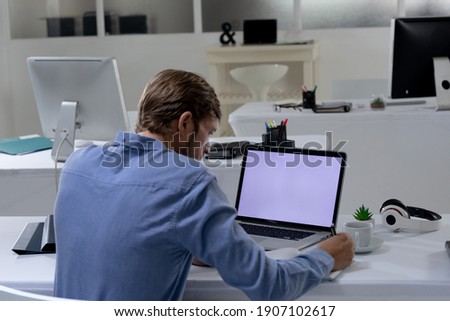 Caucasian businessman sitting at desk using laptop in an empty office. working online, social distancing in the workplace during quarantine lockdown.