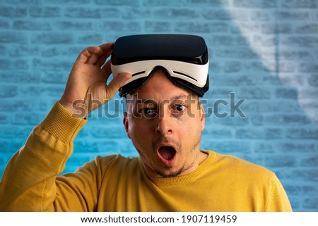 Excited man experiencing virtual reality via VR headset isolated on blue neon background. Man looking though VR device
