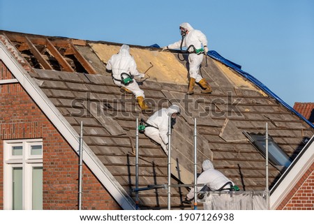 Professionals in protective suits remove asbestos-cement roofing underlayment Royalty-Free Stock Photo #1907126938