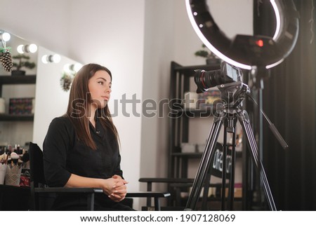 Young beautiful woman and professional beauty make up artist vlogger recording makeup tutorial in beuty studio to share on website or social media. Blogger use digital camera on tripod and ring lamp