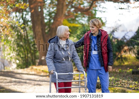 Senior woman with walking frame and caregiver outdoors on a walk in park. Royalty-Free Stock Photo #1907131819