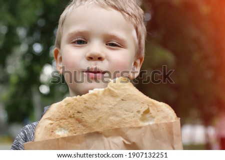 Funny blondheared toddler eating pita bread with appetite on the street and looks at the camera.Closeup photography of cute boy with .Copy space for text.