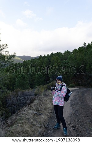 Young and attractive female with a colourful jacket taking landscape photos in a forest with a digital camera.