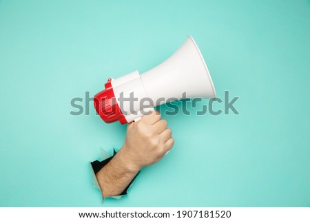 Male hand arm hold megaphone isolated through torn blue background Royalty-Free Stock Photo #1907181520