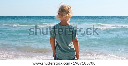 Little boy walking and playing alone on the beach. Summertime, vacation, travel, nature banner.