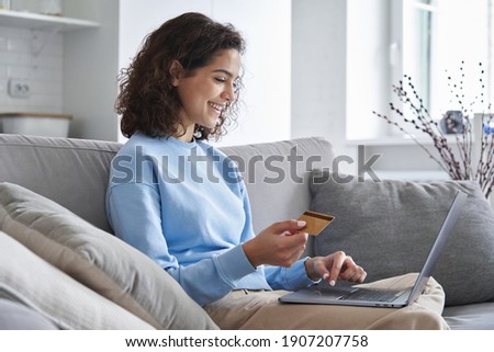 Happy hispanic young woman consumer holding credit card and laptop buying online at home. Female shopper customer shopping on ecommerce website market place making digital payment using bonus money. Royalty-Free Stock Photo #1907207758