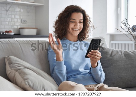 Happy hispanic teen girl waving hand using smartphone app enjoying online virtual chat video call with friends in distance mobile chat virtual meeting, recording stories for social media at home. Royalty-Free Stock Photo #1907207929