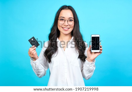 Elegant cute Asian girl in a white blouse, holds in her hand a credit card for registration on the application site. Business woman paying with a credit card for purchases on the Internet.