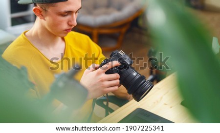young guy photographer, videographer sets up camera, views photos and videos on camera at home. young man processes photos and videos. in program editor. Freelancer. Remote work. Retouching training