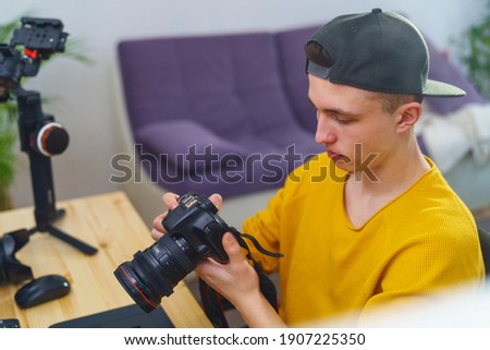 young guy photographer, videographer sets up camera, views photos and videos on camera at home. young man processes photos and videos. in program editor. Freelancer. Remote work. Retouching training
