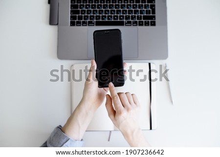 Young women is holding black smartphone over laptop.