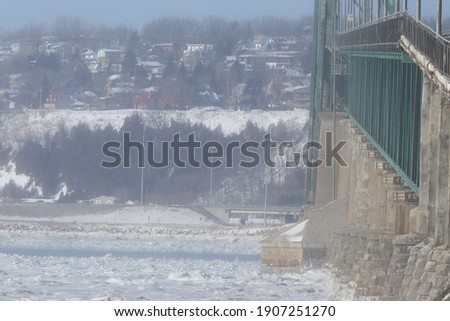 view of a viaduct in winter with ice on the St. Lawrence river in Quebec and houses in the background
